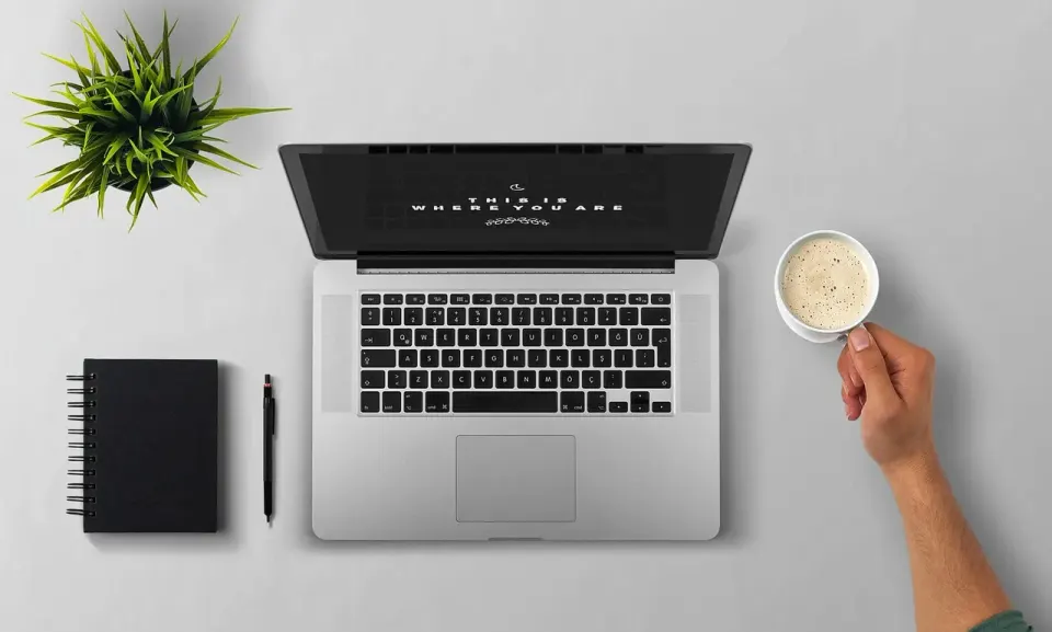 A person using a laptop at a table with a cup of coffee