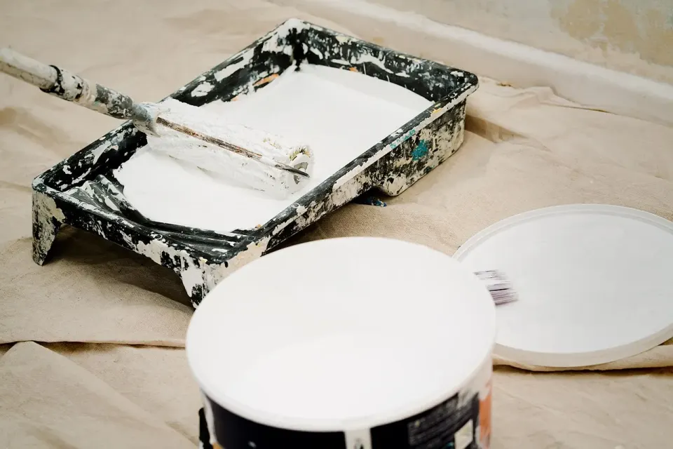 An open bucket of interior paint with a brush resting on top