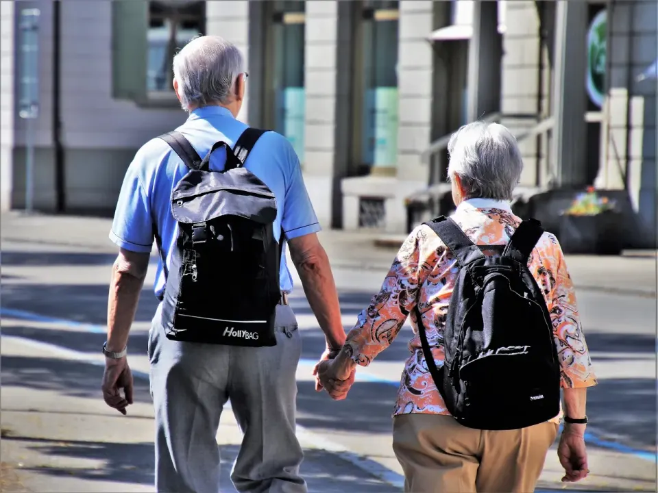 Older couple with backpacks walking hand in hand down a city street