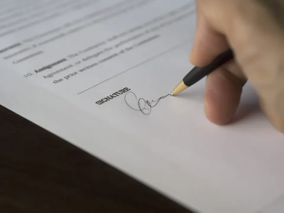 Hand signing a printed contract with a pen on the signature line