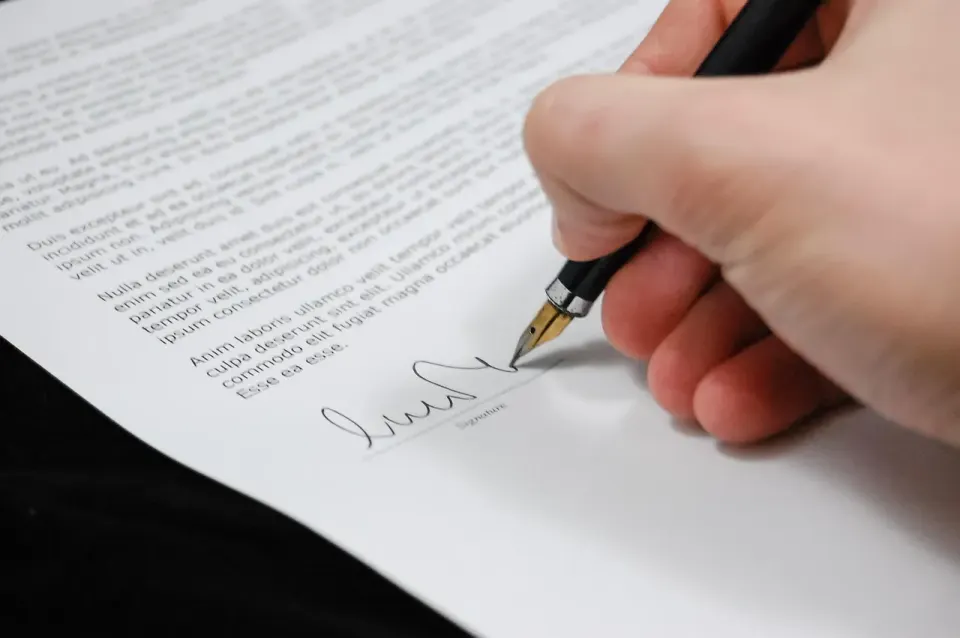 Person signing a document with a pen