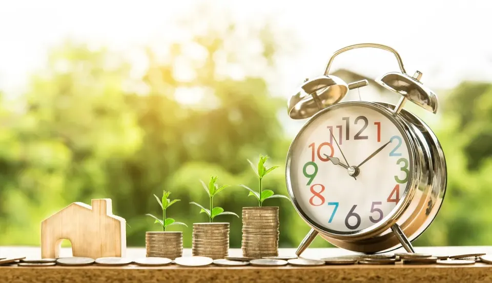 Stacks of coins with small plants growing from them beside an alarm clock