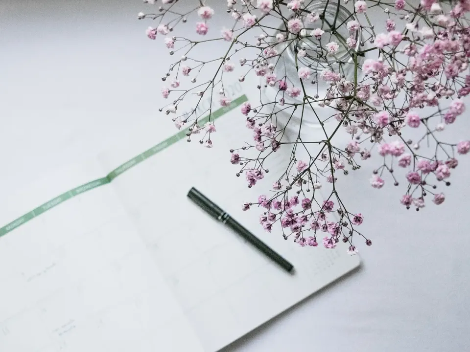Open planner and pen on a table beside pink flowers